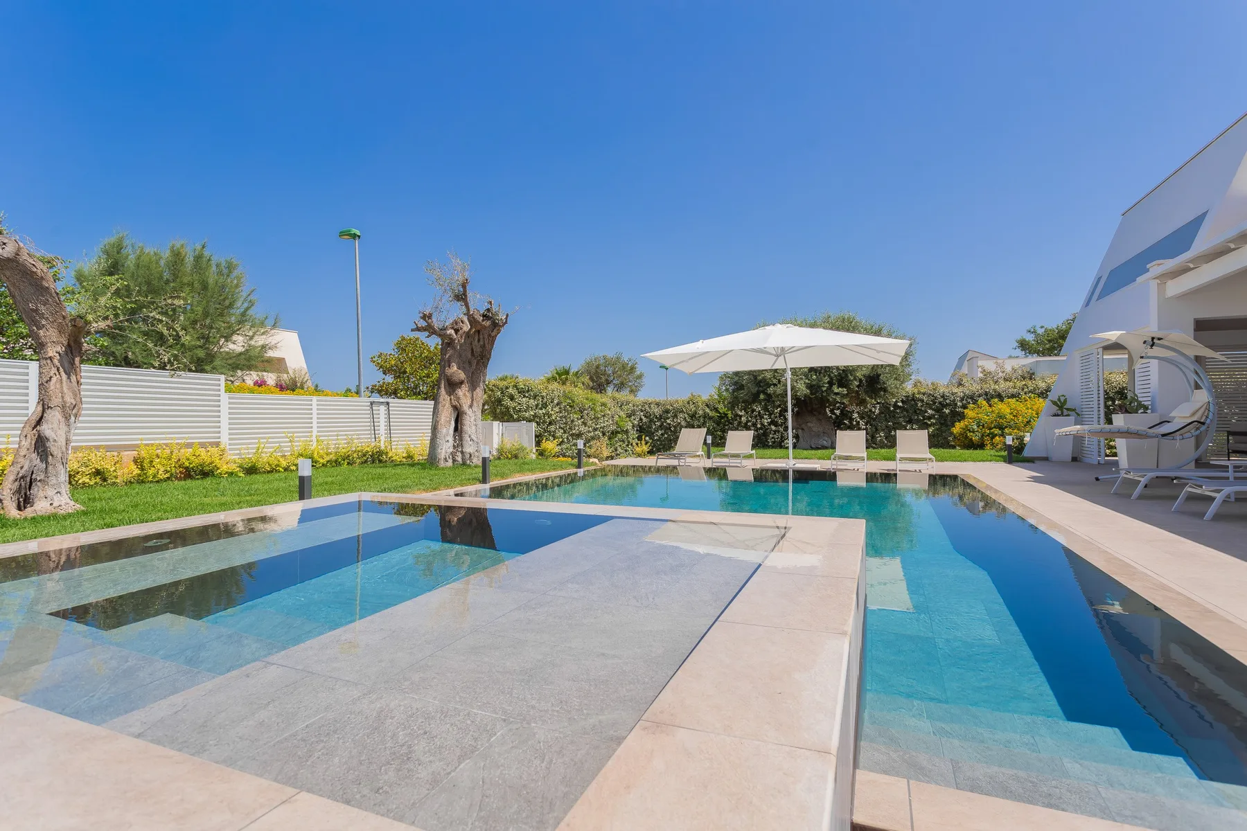 Una piscina al aire libre con una zona poco profunda y una gran sombrilla.