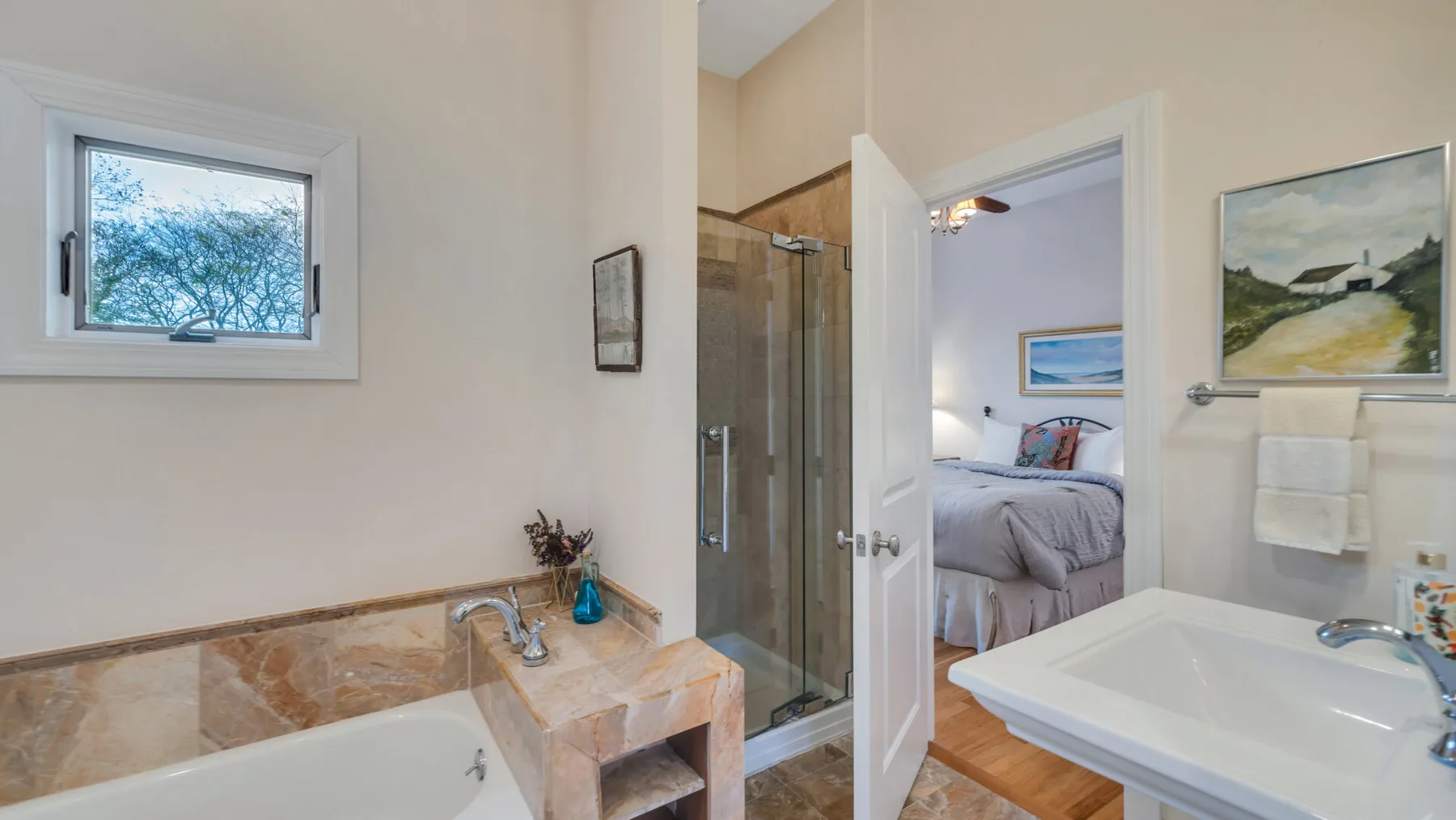 Un baño con bañera, lavabo y una puerta abierta hacia un dormitorio.