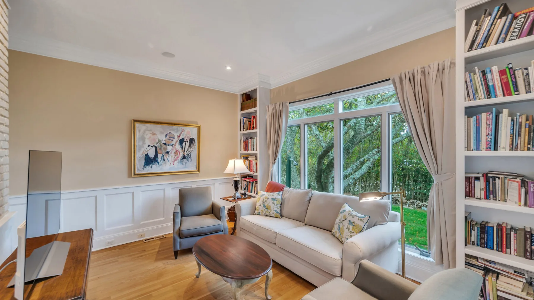 Una luminosa sala de estar con sofá, sillón y grandes ventanas con vistas a la vegetación.