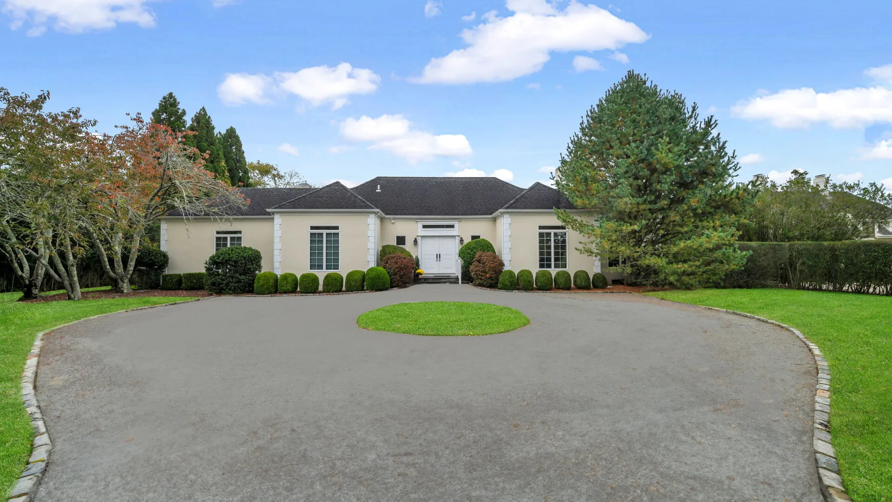 A single-story house stands beyond a broad circular driveway and landscaped lawn.