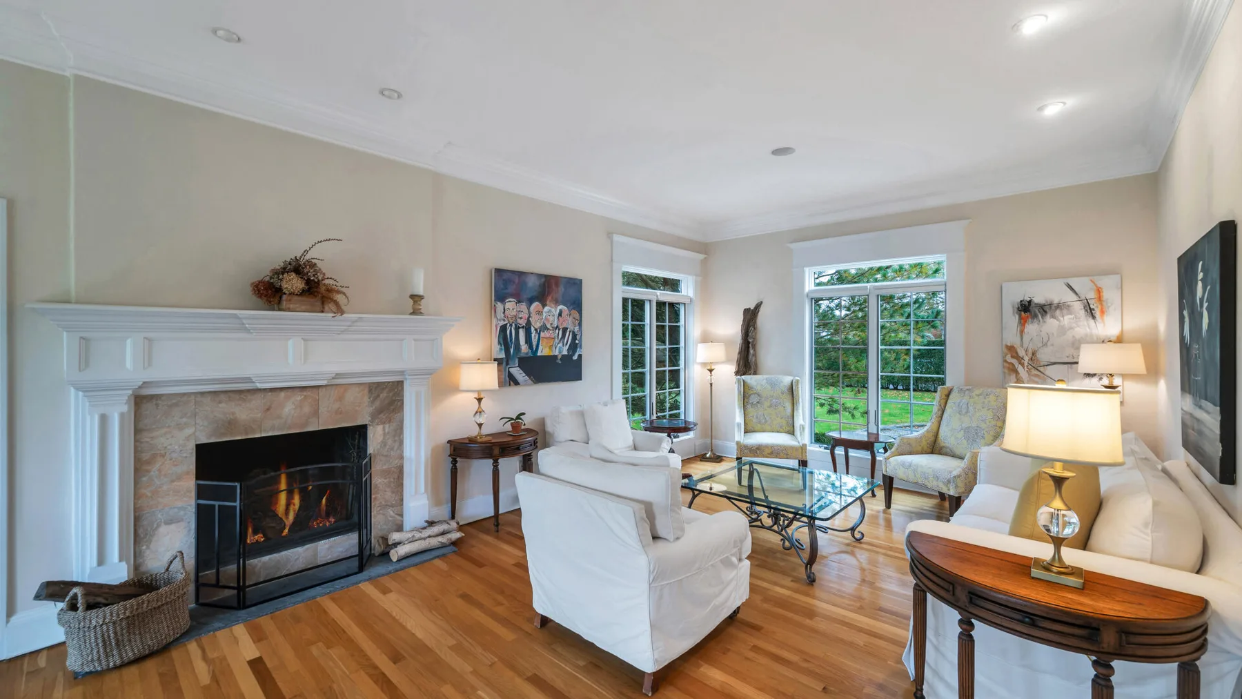 A bright living room with a fireplace, seating, and windows overlooking a garden.