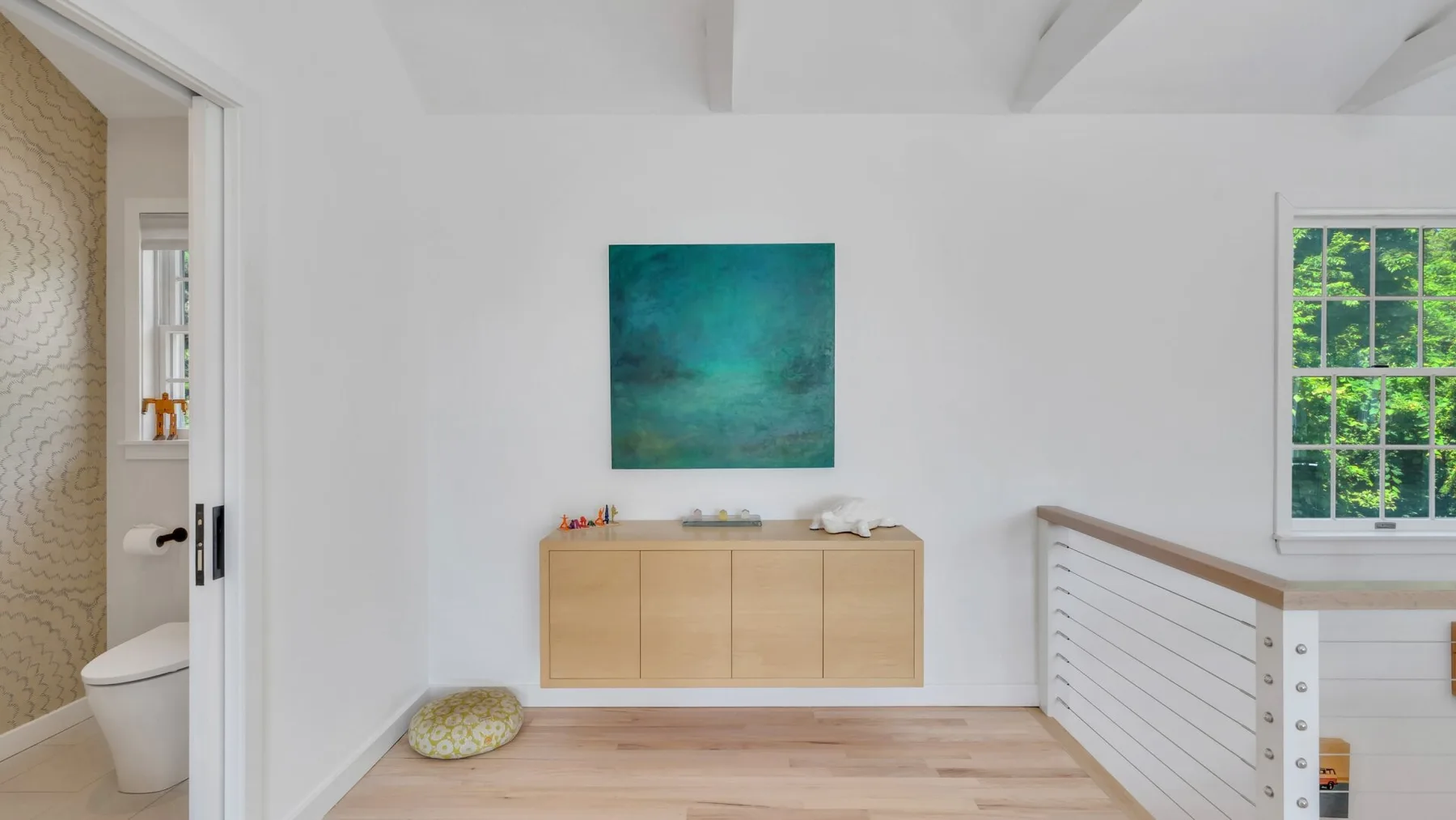 Un pasillo luminoso con un mueble de madera bajo una pintura colorida.