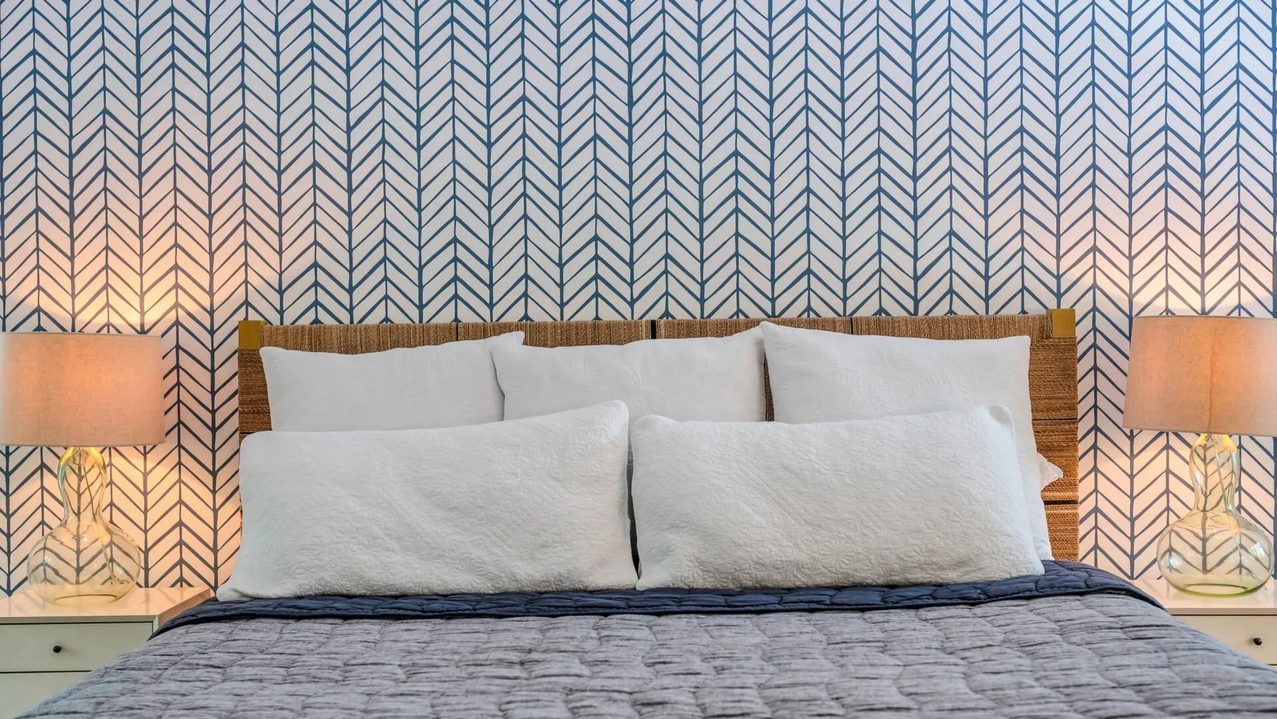Un dormitorio con una cama bien tendida y papel tapiz estampado.
