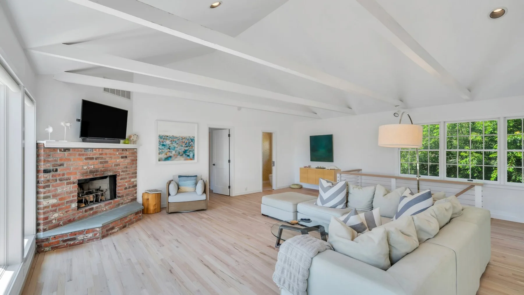 Una sala luminosa con asientos claros, una chimenea de ladrillo y grandes ventanas.