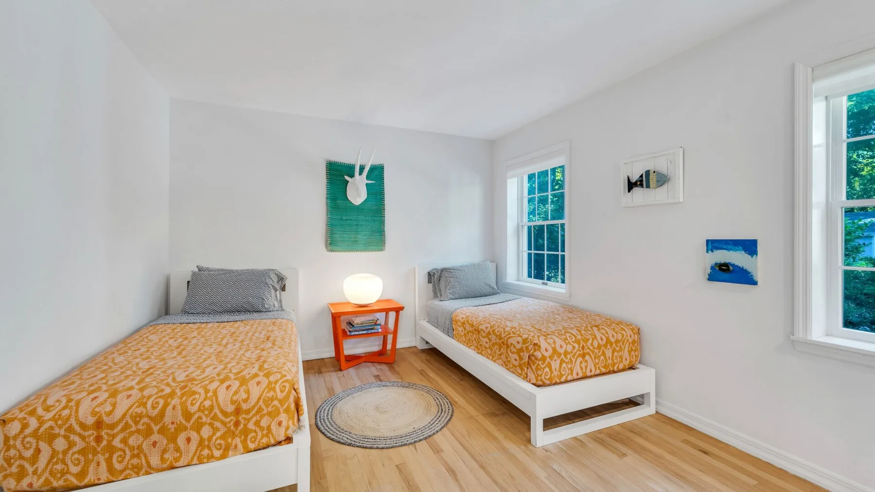 Un dormitorio luminoso con dos camas, ropa de cama estampada en tonos mostaza y ventanas grandes.