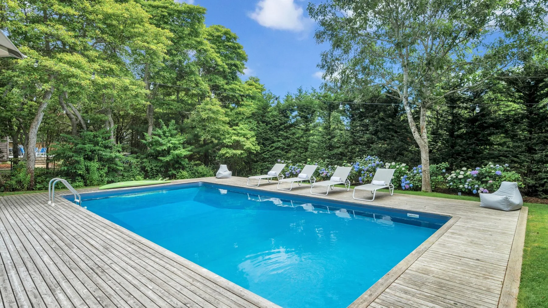 Una piscina al aire libre está rodeada por una terraza de madera y árboles frondosos.