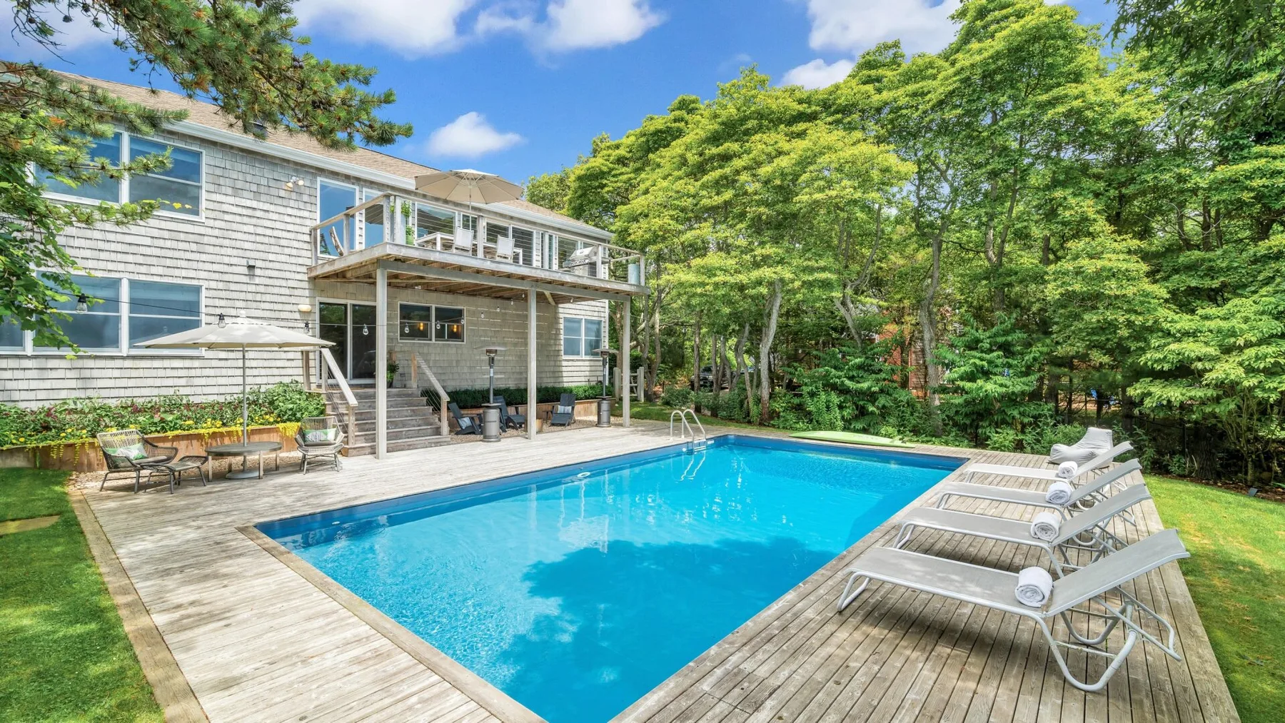 Una piscina al aire libre está junto a una casa grande y una terraza de madera.