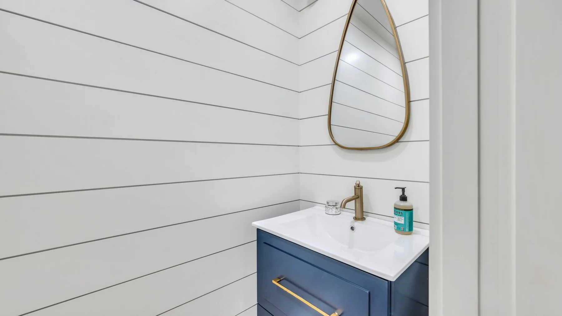 Un tocador de baño con encimera blanca, mueble azul y espejo de pared.