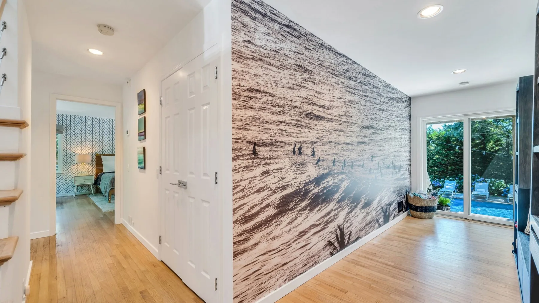 Un pasillo interior luminoso da a una habitación con un mural grande y ventanas orientadas al jardín.