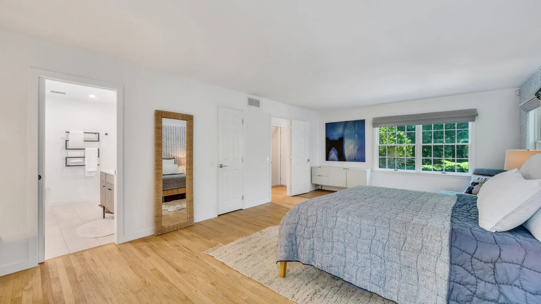 Un dormitorio luminoso con una cama grande y ventanas con vistas a la vegetación.