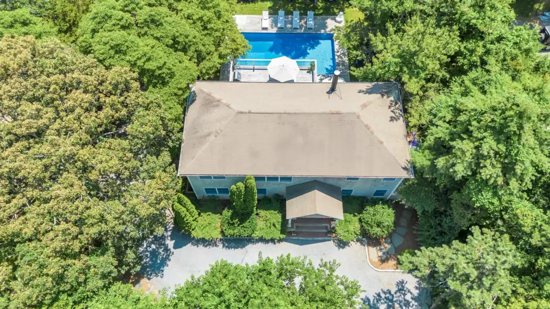 Vista aérea de una casa rodeada de árboles, con una piscina detrás.