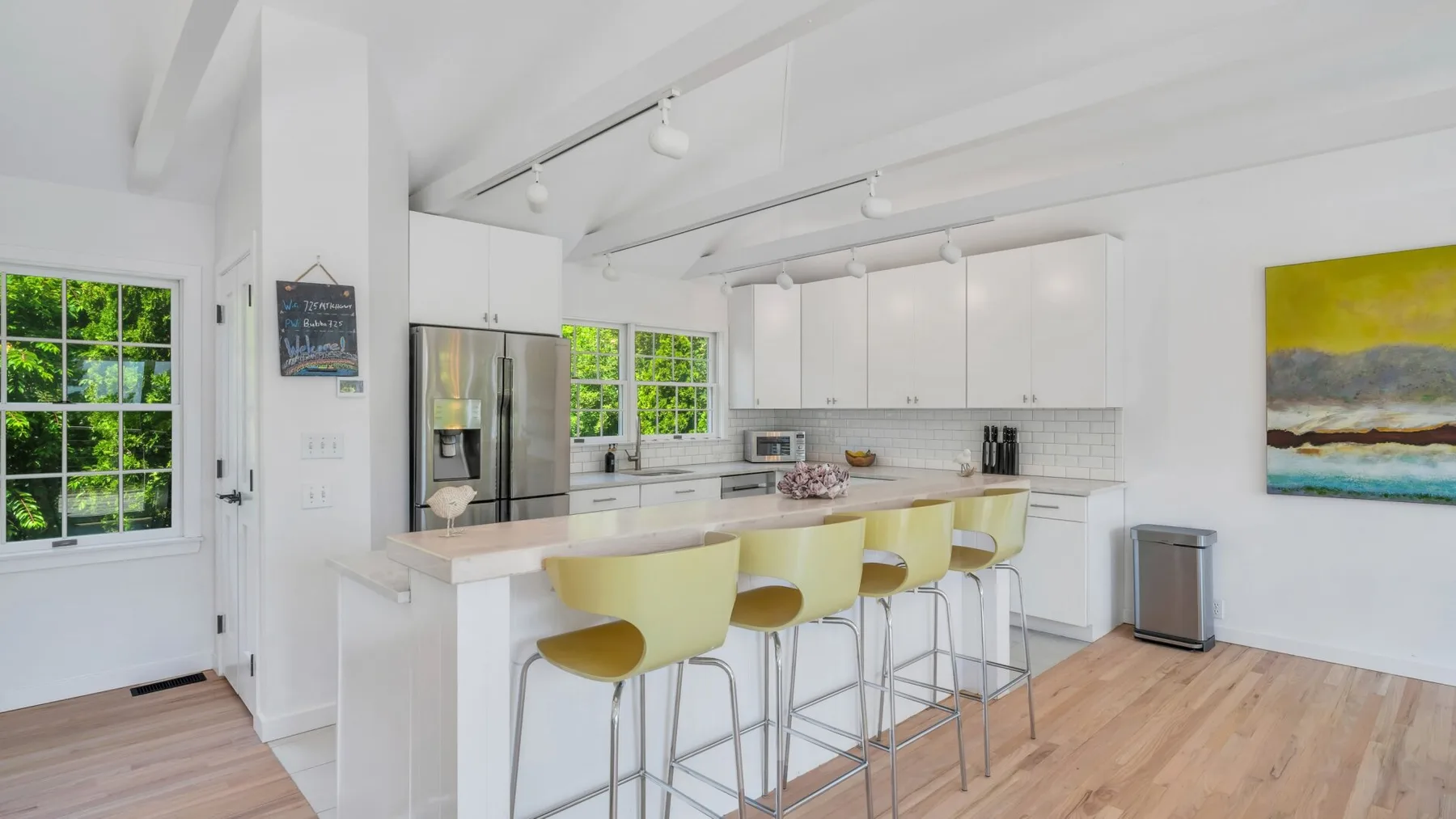Una cocina luminosa con una isla larga, asientos amarillos y ventanas grandes.