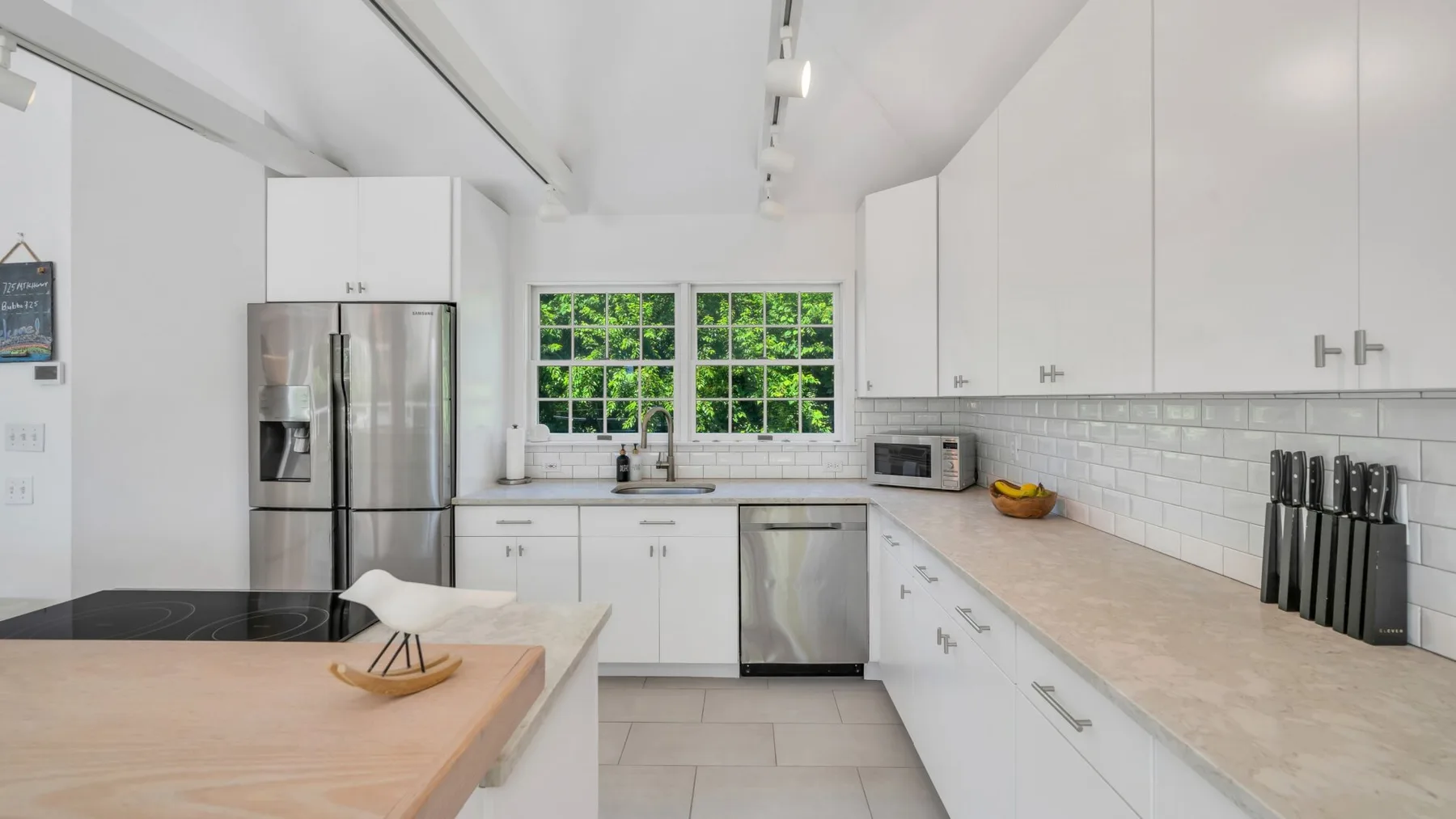 Una cocina luminosa con gabinetes blancos, una isla central y ventanas sobre el fregadero.