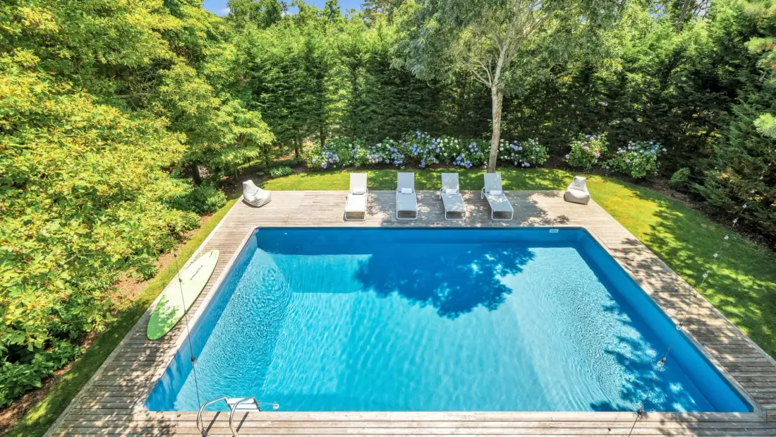 Una piscina está en un jardín ajardinado rodeado de árboles.