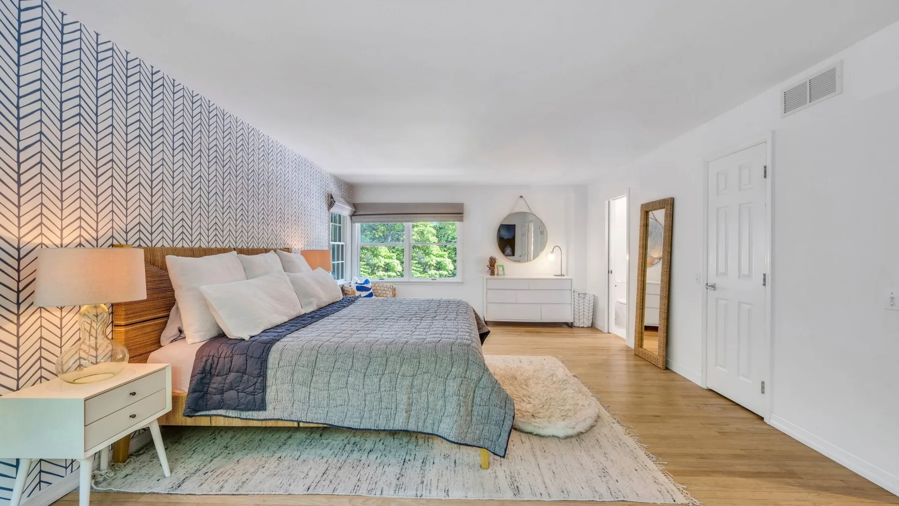 Dormitorio con una cama, papel tapiz estampado y una ventana con vista a la vegetación.
