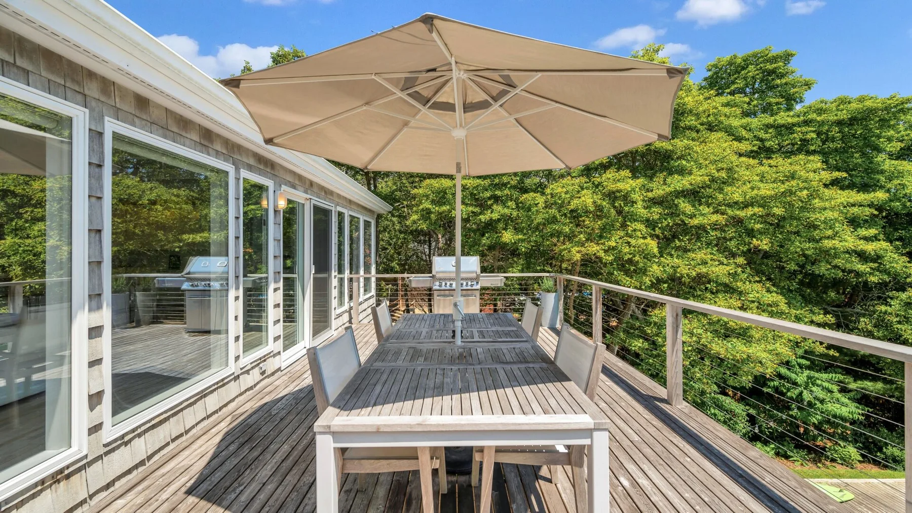 Una terraza exterior con una mesa de comedor larga bajo una sombrilla grande.