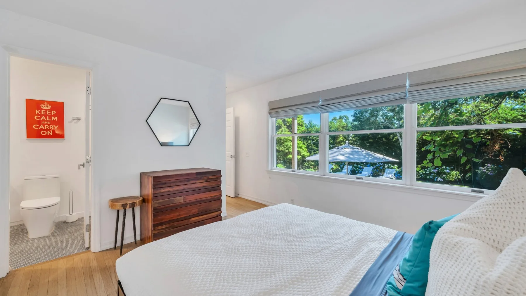 Un dormitorio luminoso con una cama bien tendida y amplias ventanas con vistas a la vegetación.