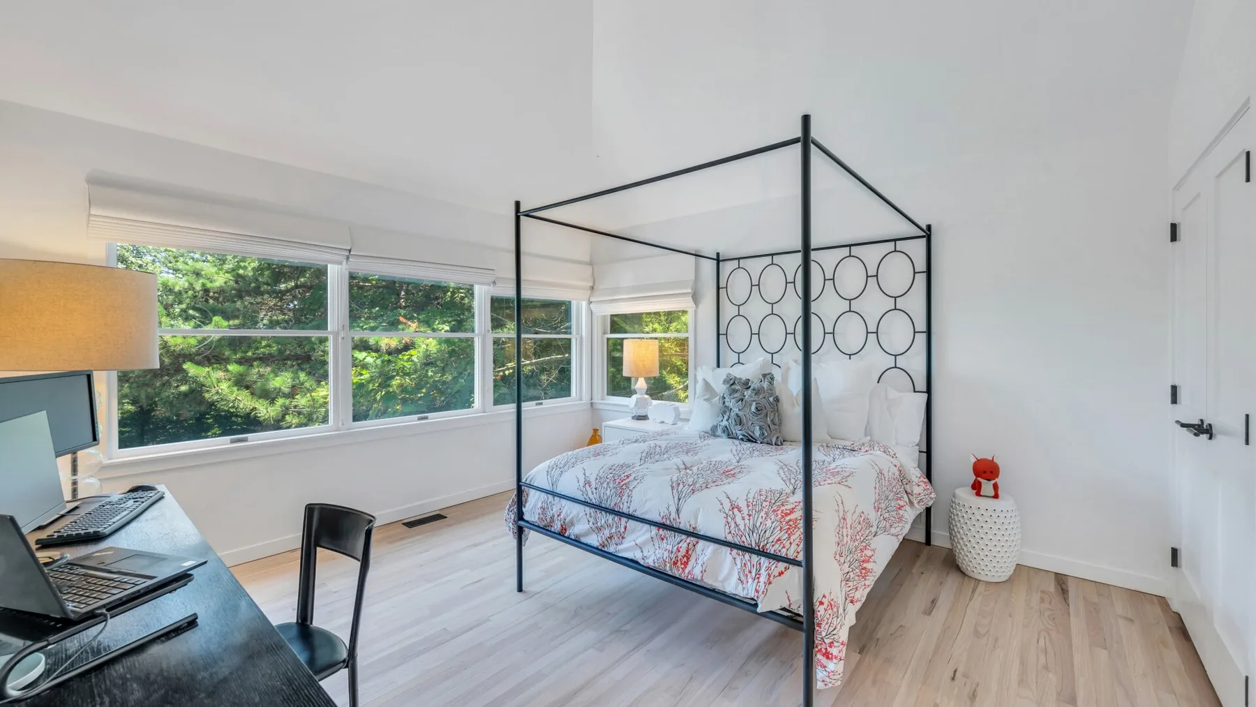 Un dormitorio luminoso con una cama floral junto a amplias ventanas con vistas a la vegetación.