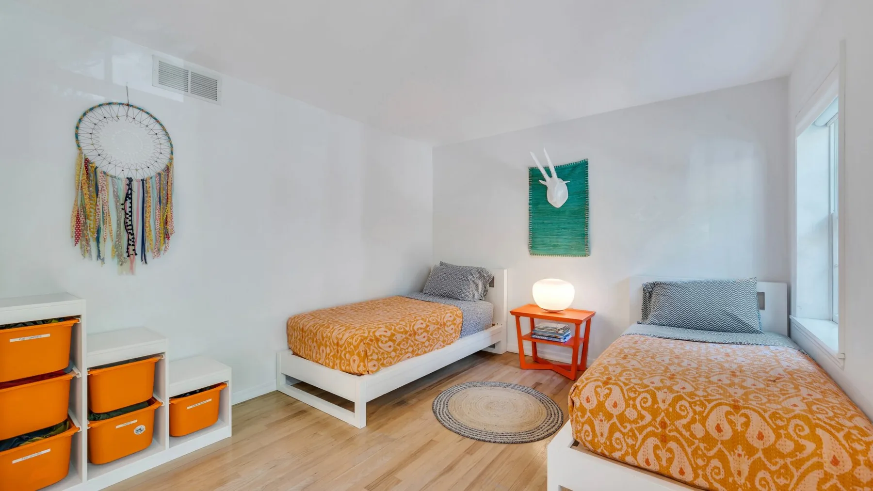 Un dormitorio luminoso con dos camas, ropa de cama estampada naranja y una mesita entre ellas.
