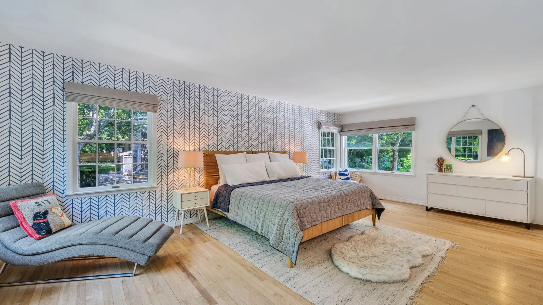 Un dormitorio con una cama, papel tapiz estampado y una chaise longue.