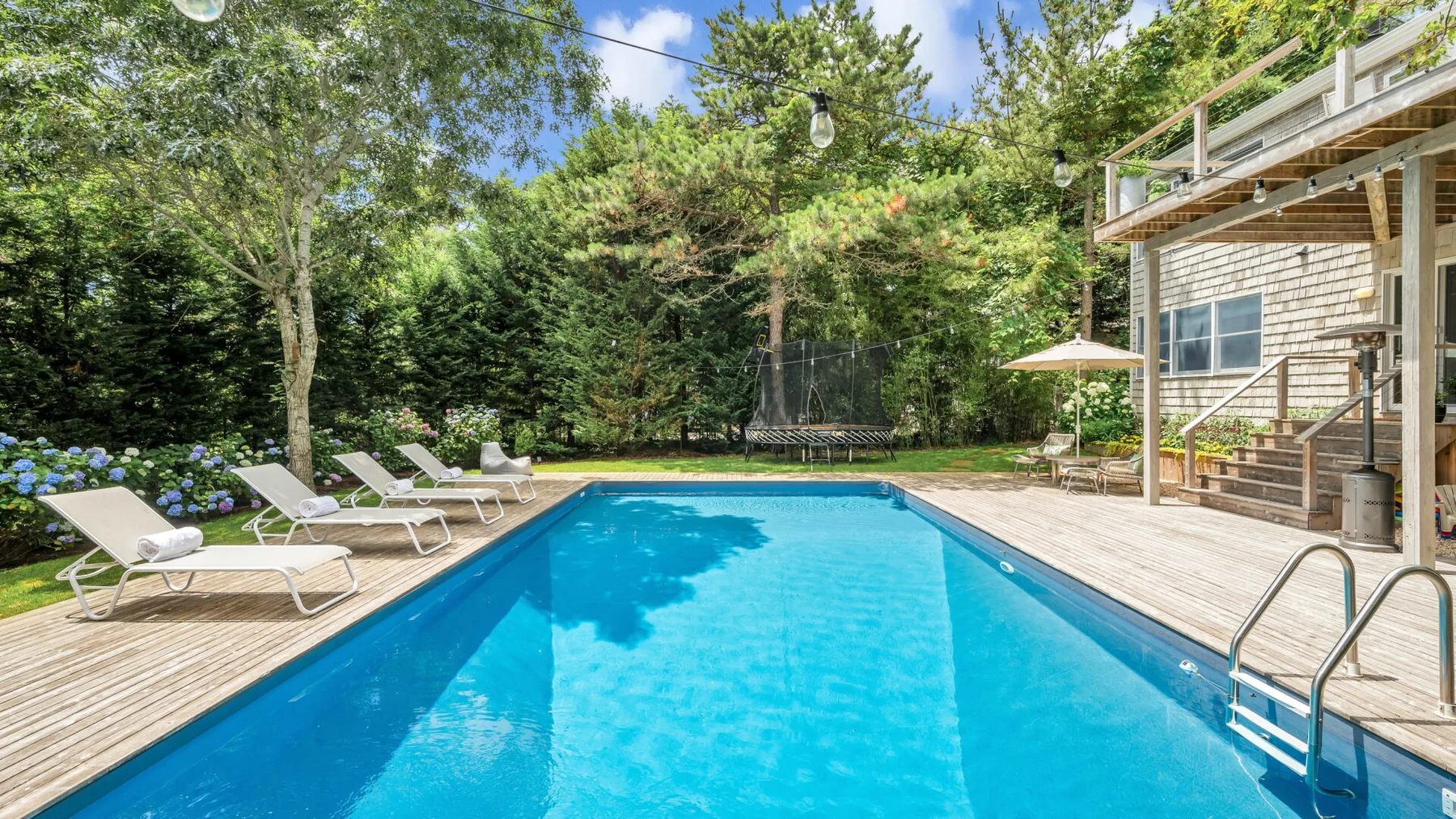 Una piscina al aire libre junto a una terraza de madera y una casa.