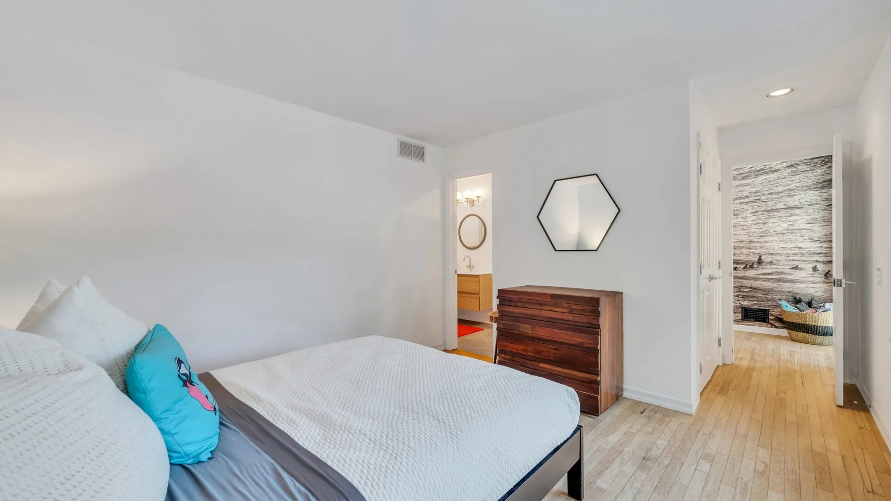 Un dormitorio con una cama y una cómoda de madera bajo un espejo hexagonal.
