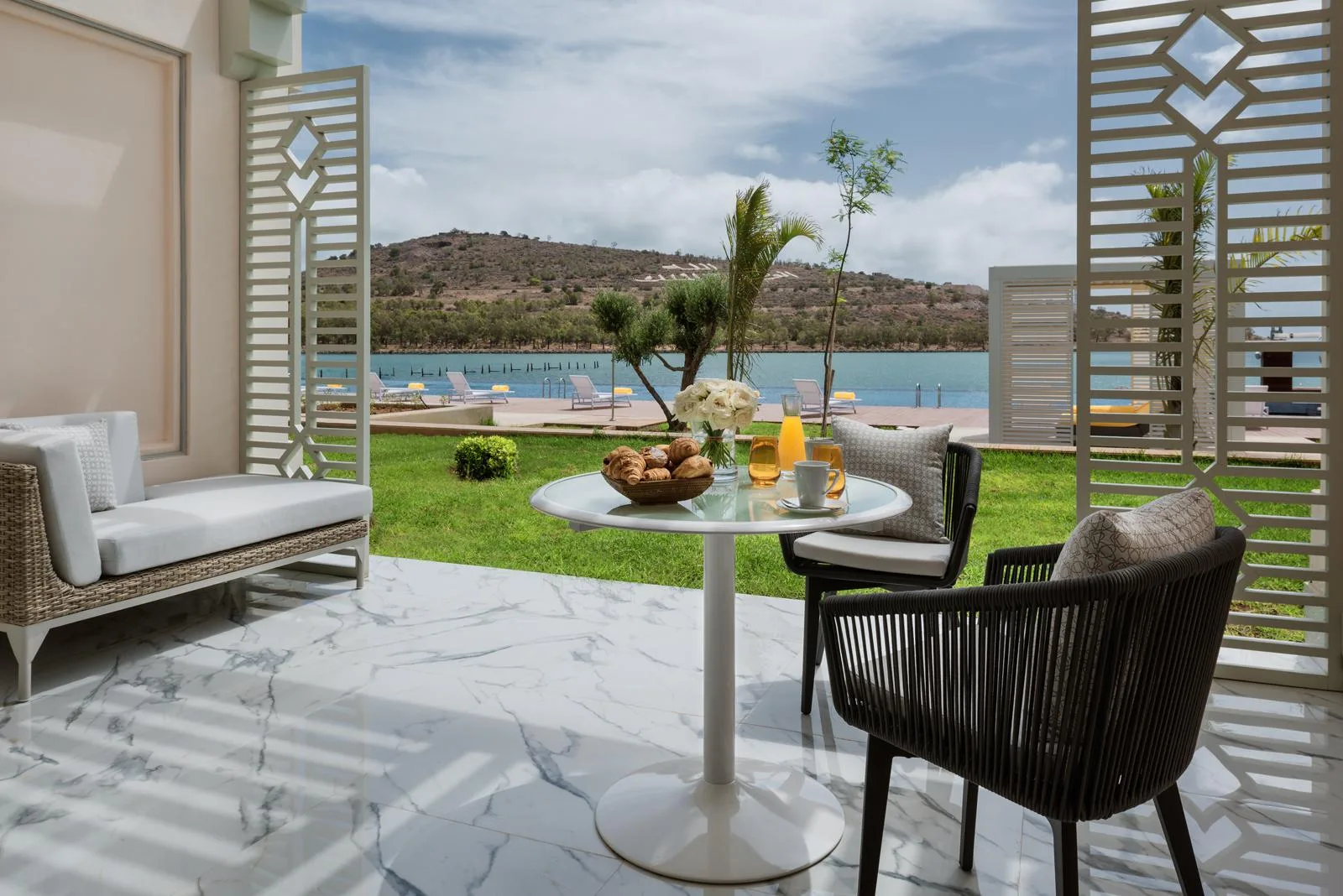 Terraza con mesa, sillas y sofá con vistas a una zona de césped y a la laguna.