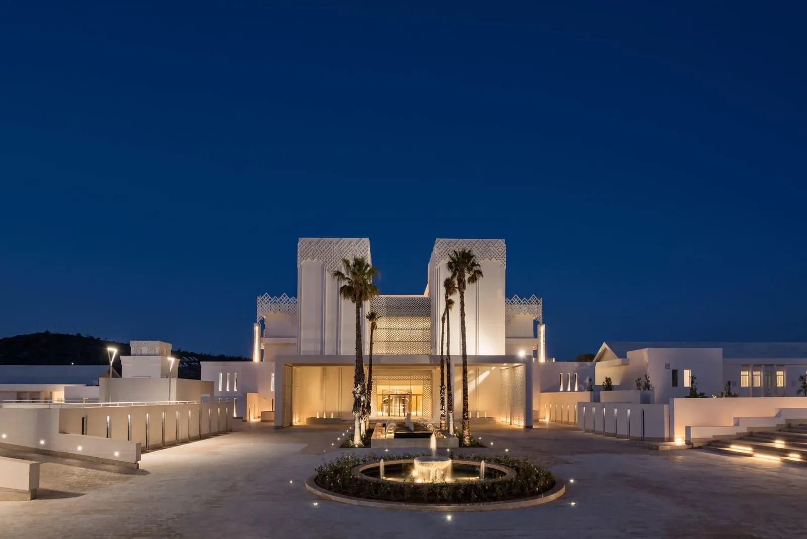 Exterior del Marchica Lagoon Resort de noche, con un patio central, una fuente y palmeras.