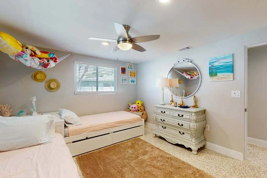 Un dormitorio luminoso con camas, una cómoda y un ventilador de techo.