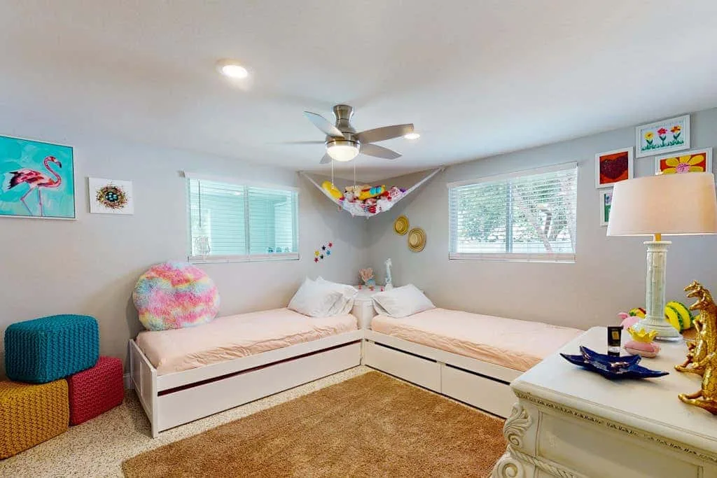 Un dormitorio luminoso con dos camas en forma de L bajo un ventilador de techo.