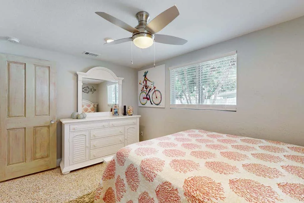 Un dormitorio con una colcha estampada, una cómoda y una ventana.