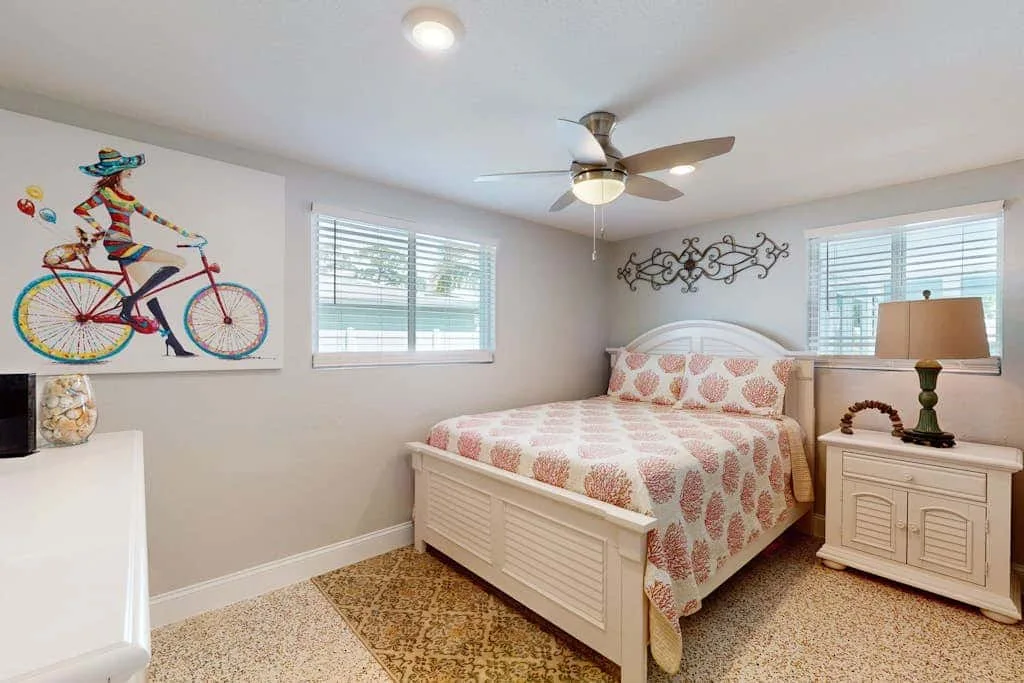 Un dormitorio con una colcha estampada, arte decorativo en la pared y dos ventanas.