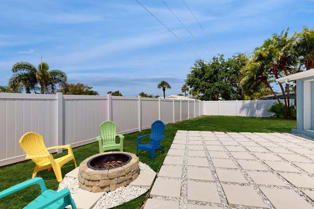 A paved backyard patio beside a fenced lawn and circular fire pit.