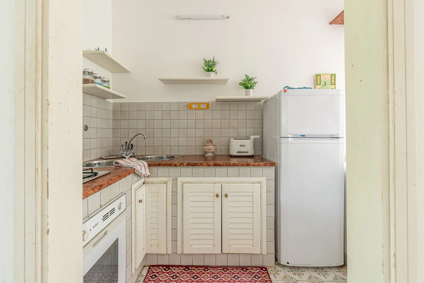 A small kitchen with tiled walls, a counter, and a refrigerator.