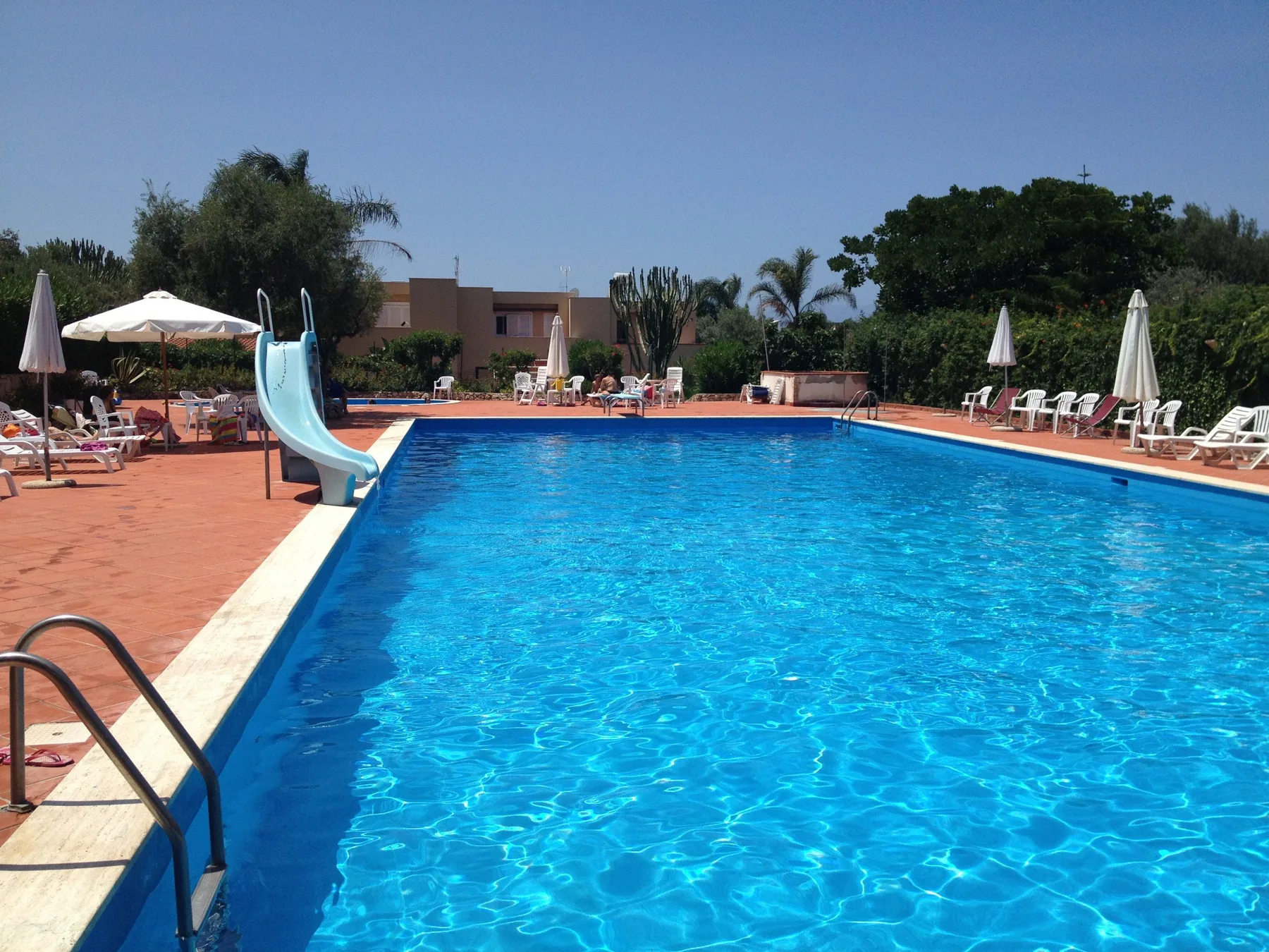 An outdoor swimming pool is surrounded by lounge seating and umbrellas.
