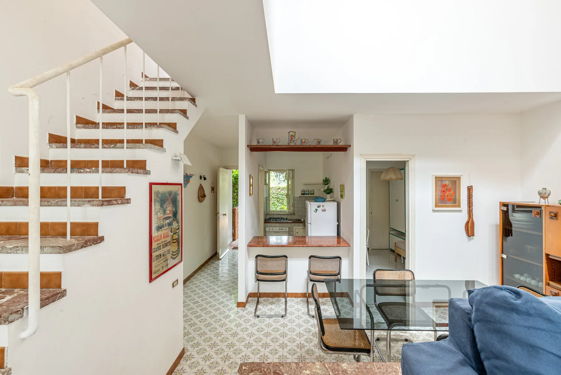 Open-plan living area with a dining table, blue seating, and a kitchen beyond.