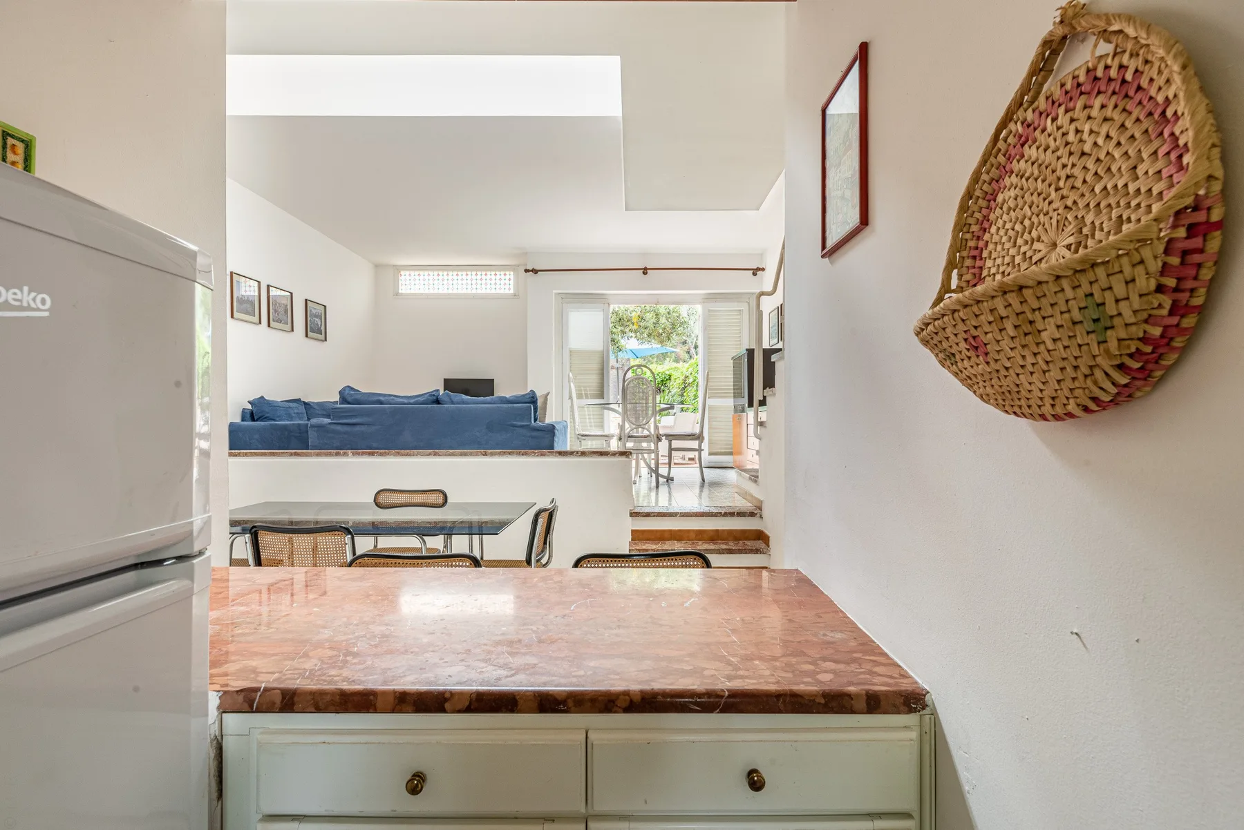 A kitchen counter looks toward a dining area and blue seating in the adjoining room.