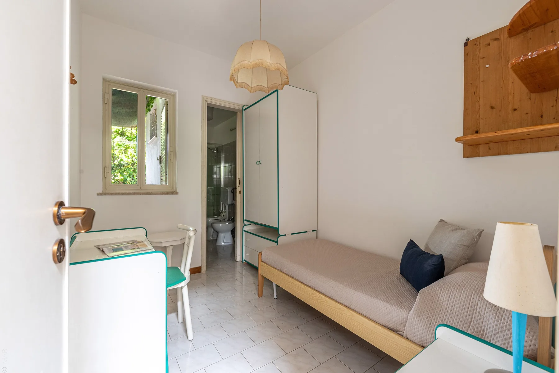 A bright room with a single bed, a small table, and a window.
