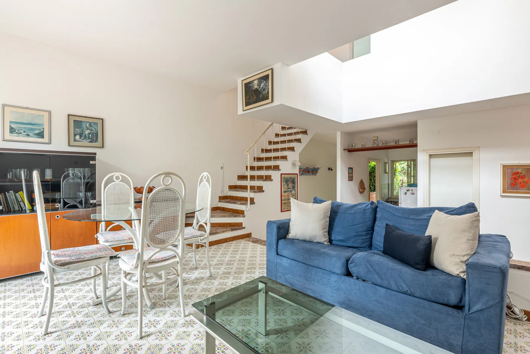 A bright living and dining area with a blue sofa and glass coffee table.