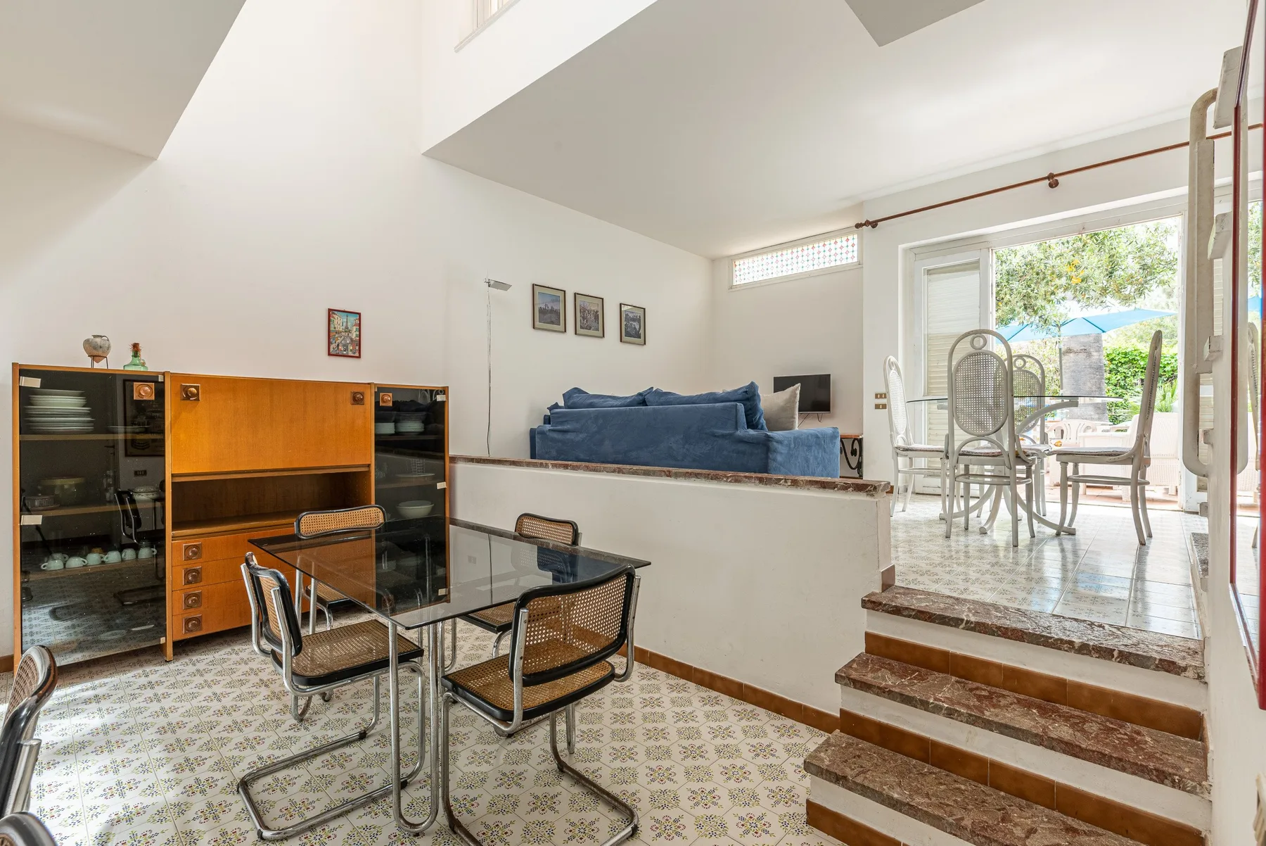 A bright living room with raised seating, a glass table, and doors opening to a patio.