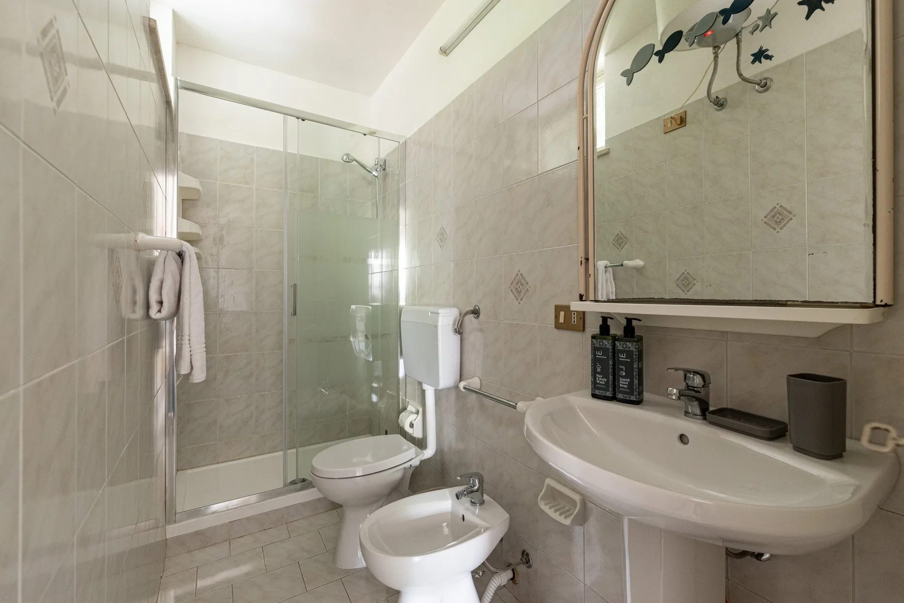 A tiled bathroom with a glass shower, toilet, bidet, and sink.