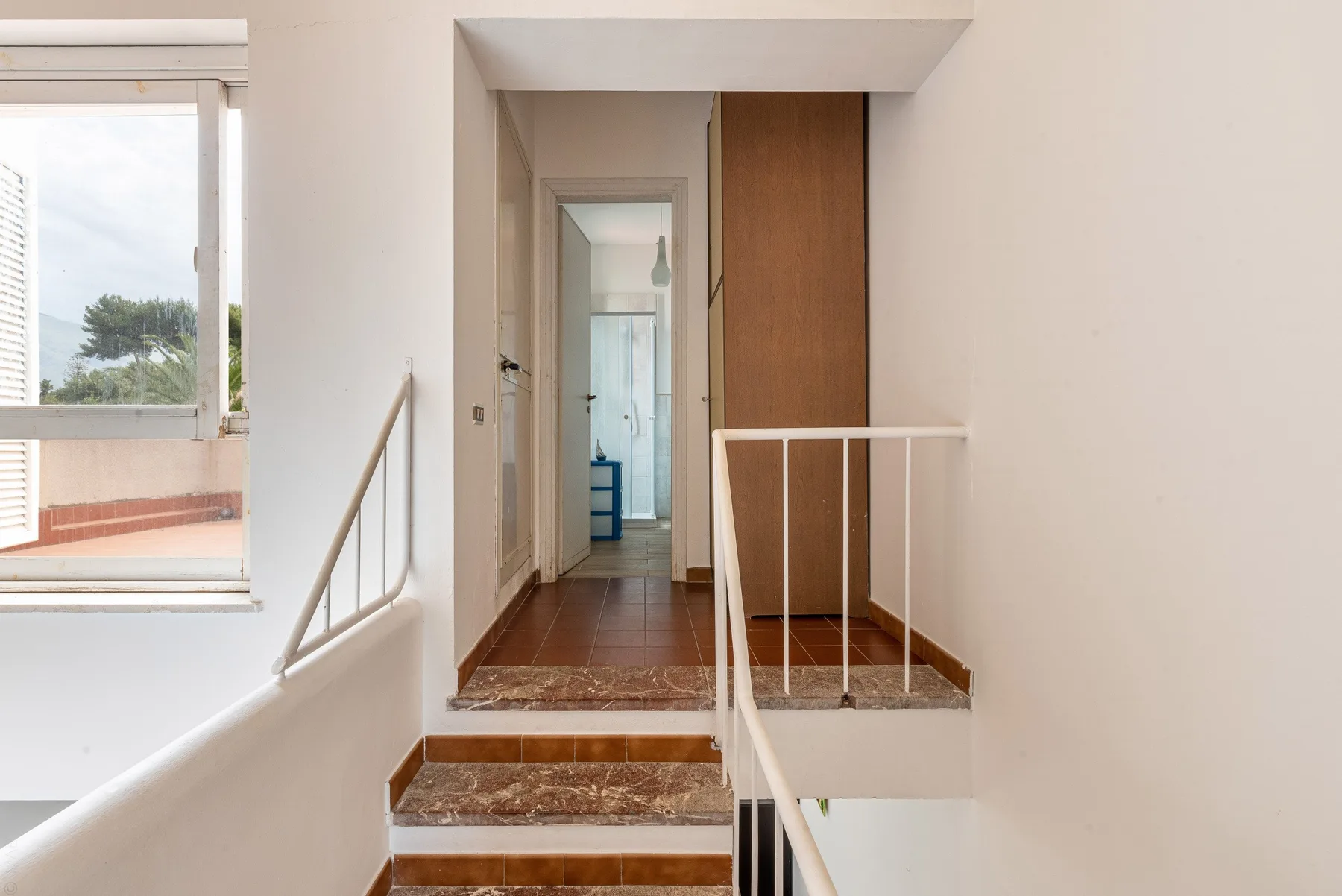 Interior hallway with tiled steps and a window overlooking greenery.