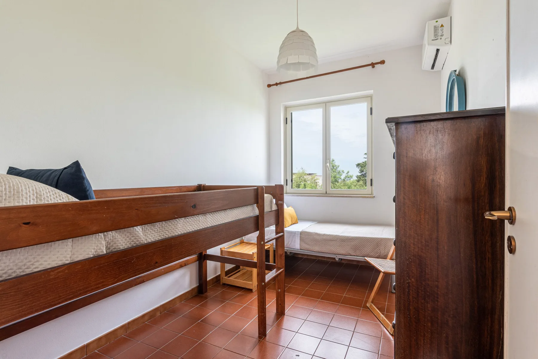 A bedroom with wooden beds, a window, and tiled flooring.