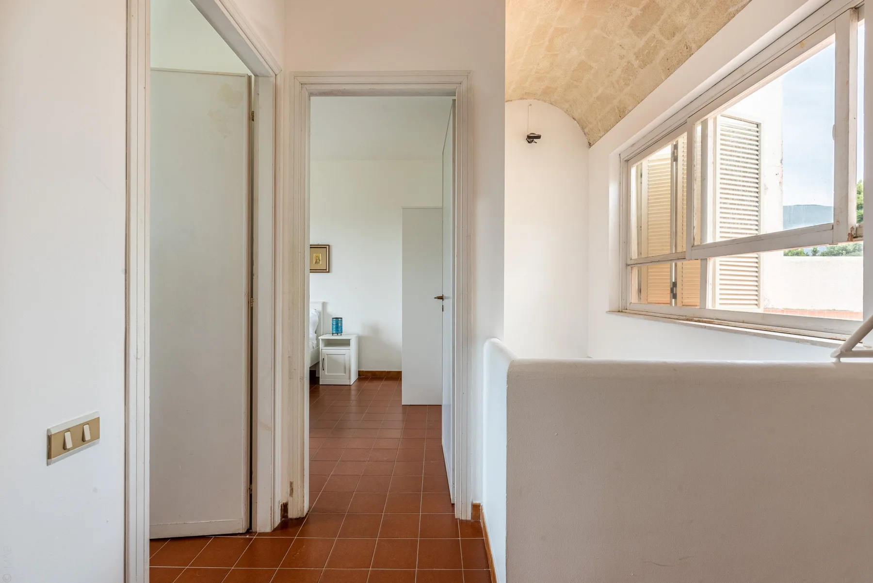 A bright hallway with terracotta-colored floor tiles and a large window.