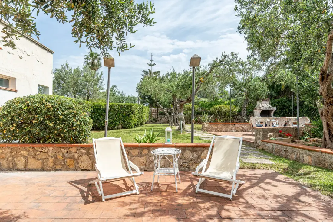 A paved garden patio with two reclining seats and greenery.