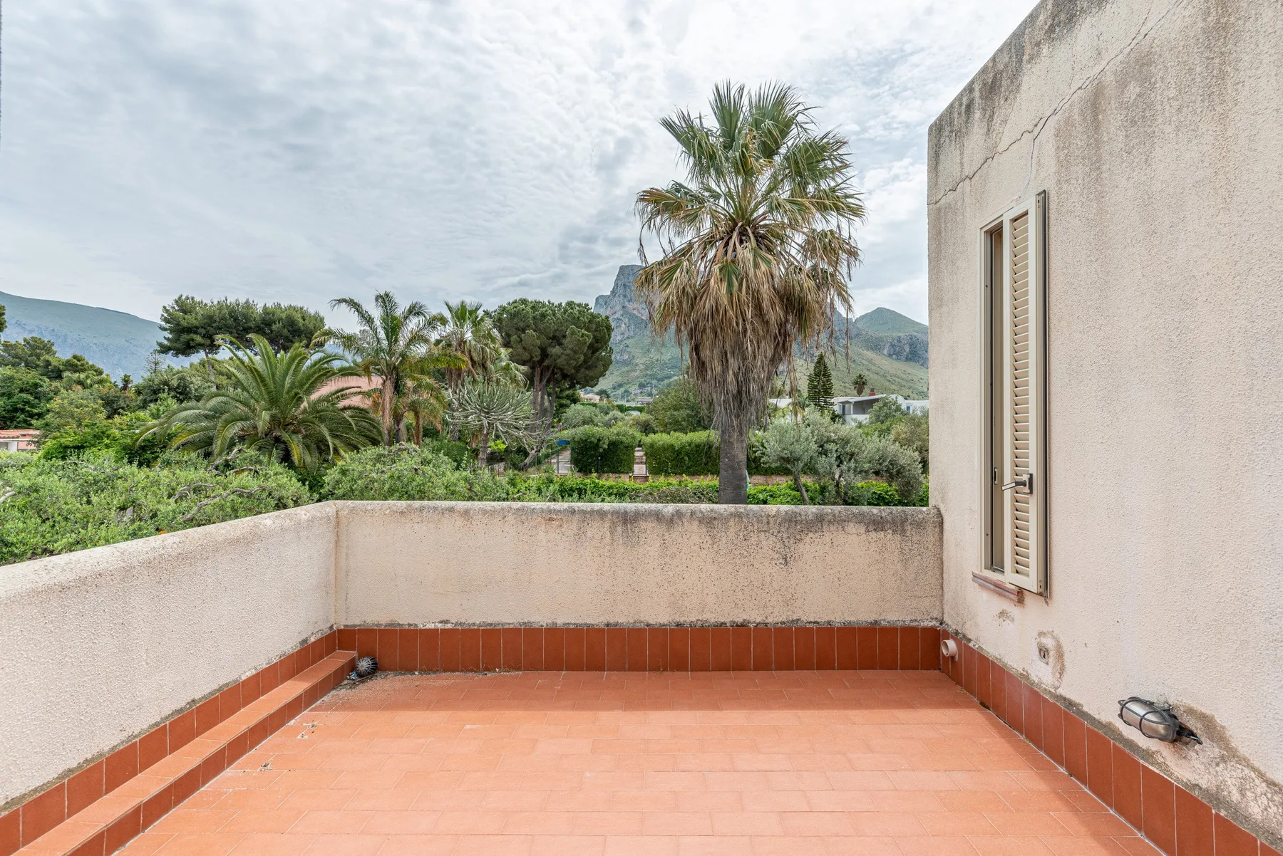 A tiled terrace overlooks a garden with palm trees and distant hills.