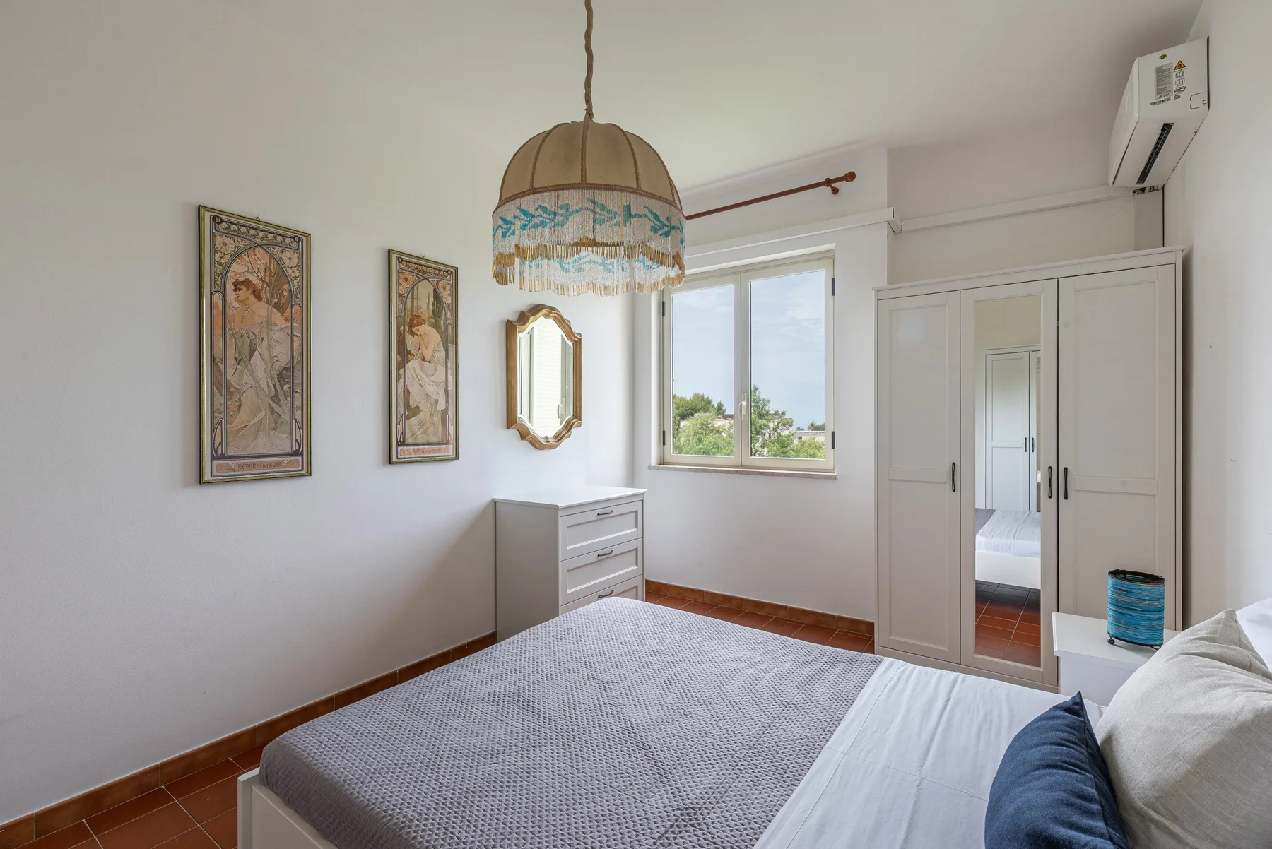 A bedroom with a bed, dresser, and window overlooking greenery.