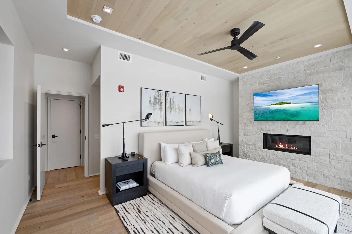 A bright bedroom with a white bed, wood ceiling, and stone accent wall.