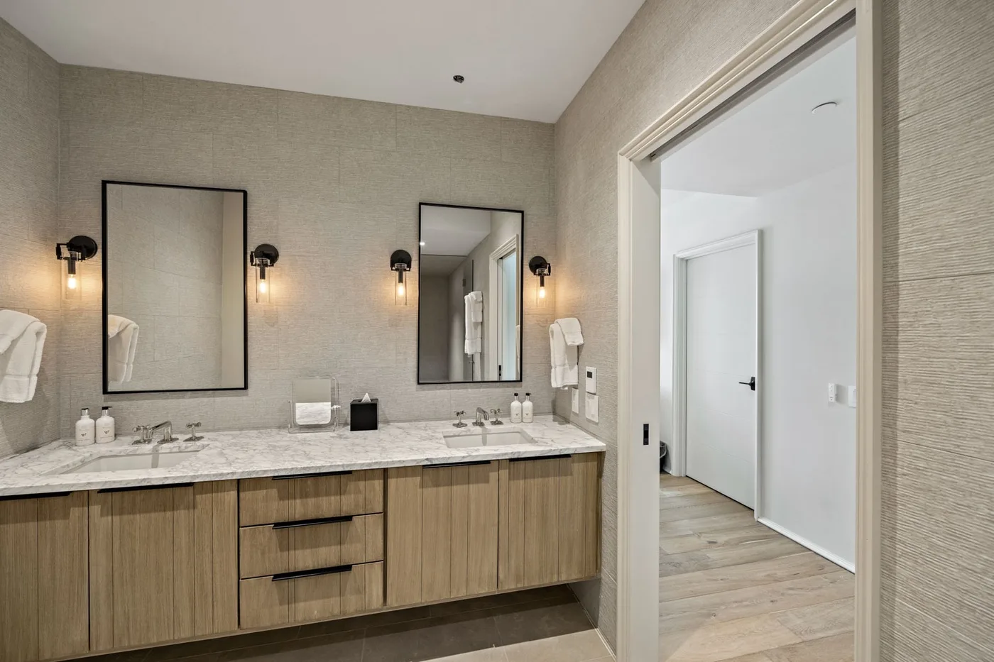 A bathroom vanity with mirrors and wall lights beside an open doorway.