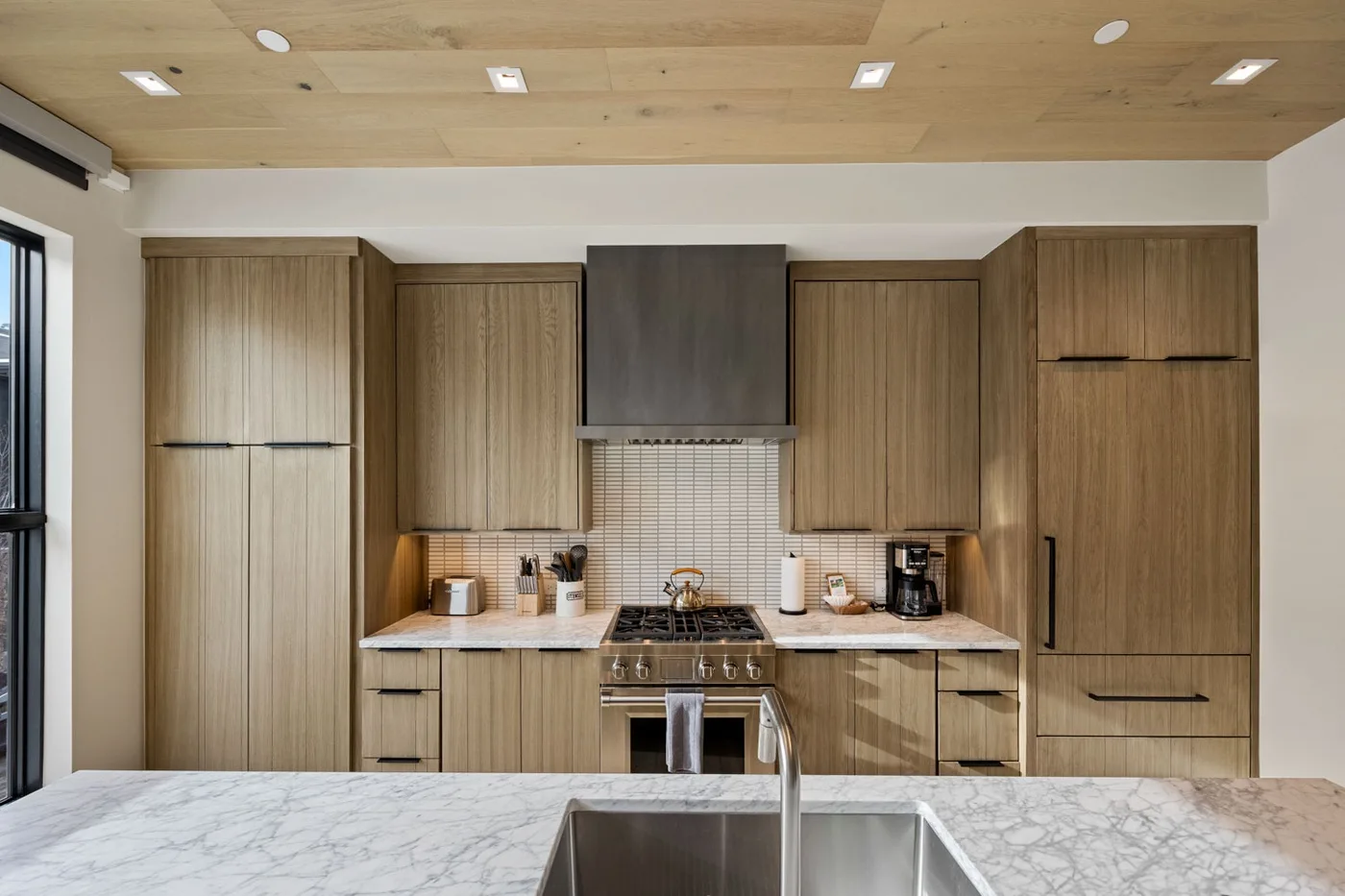 A modern kitchen with wood cabinetry, a central cooktop, and a marble-patterned island.